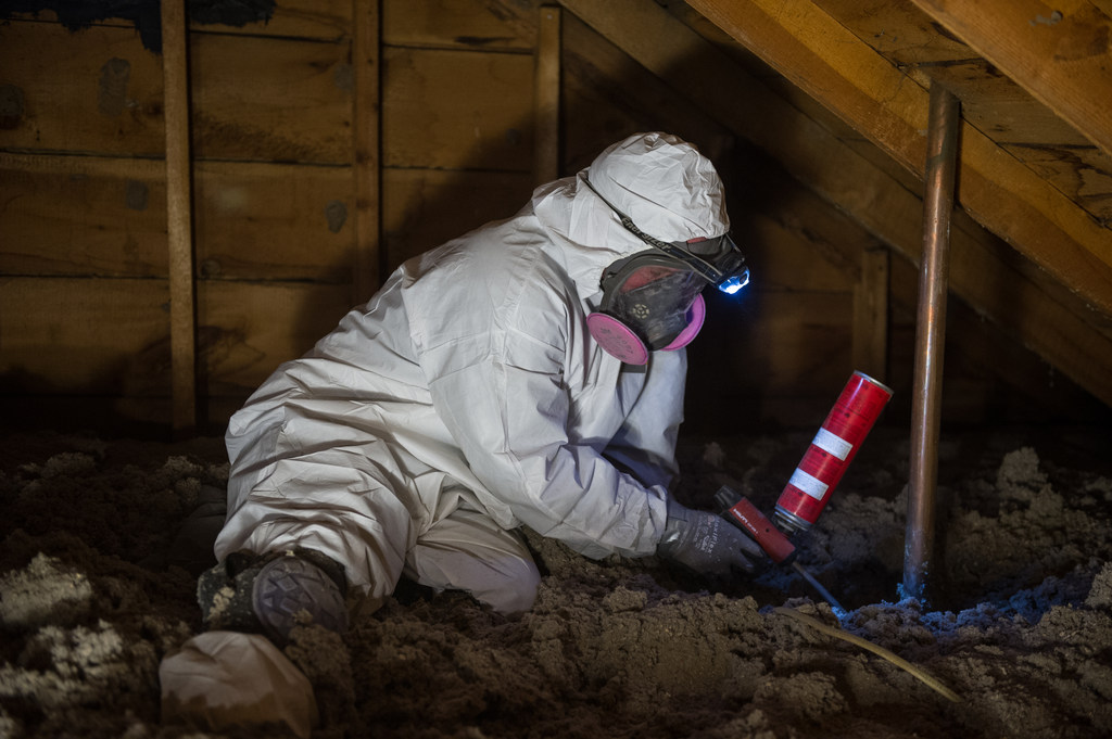 Weatherization technician air-sealing an attic, an upgrade category tied to home energy rebates and utility savings.