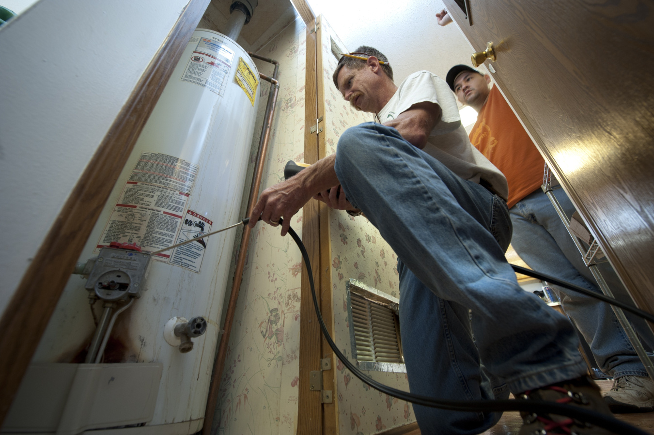 Weatherization Assistance Program technicians inspecting a residential water heater as part of home energy savings work.